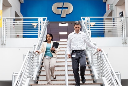 Zaměstnanci společnosti Colgate-Palmolive scházejí po schodech, za nimi je na modré zdi logo společnosti Colgate-Palmolive.