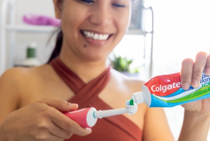 Žena, která se usmívá, zatímco v koupelně nanáší zubní pastu Colgate na zubní kartáček.
